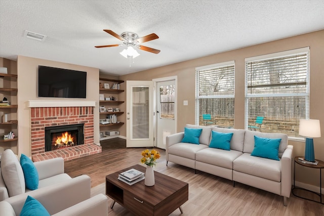 living room featuring light hardwood / wood-style flooring, a brick fireplace, a textured ceiling, and a wealth of natural light