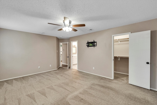 unfurnished bedroom featuring ceiling fan, a textured ceiling, light carpet, a spacious closet, and a closet