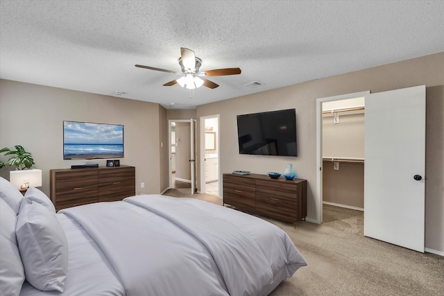 bedroom featuring ceiling fan, a textured ceiling, light carpet, a walk in closet, and a closet