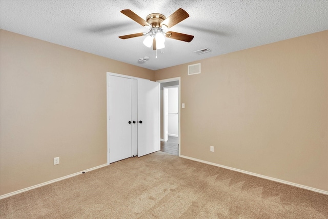 empty room featuring ceiling fan, light colored carpet, and a textured ceiling