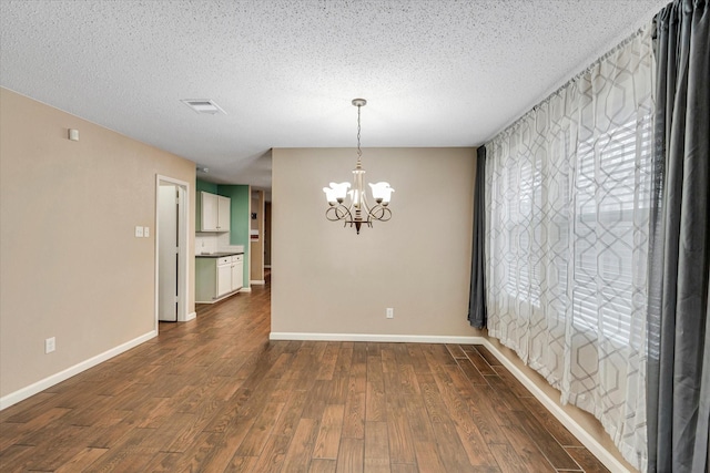 spare room with dark wood-type flooring, a notable chandelier, and a textured ceiling