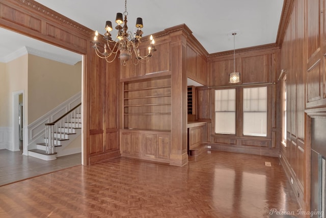 unfurnished dining area with built in shelves, wood walls, an inviting chandelier, parquet floors, and ornamental molding