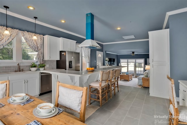 kitchen with appliances with stainless steel finishes, island range hood, sink, white cabinets, and ornamental molding