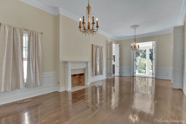 unfurnished living room featuring an inviting chandelier, ornamental molding, and hardwood / wood-style flooring