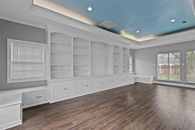 unfurnished living room featuring a raised ceiling, ornamental molding, built in features, and dark wood-type flooring