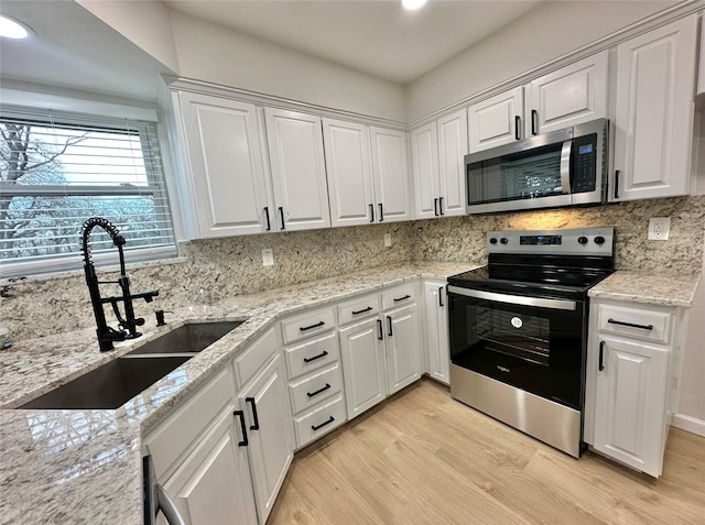 kitchen with stainless steel appliances, white cabinets, sink, and light stone countertops