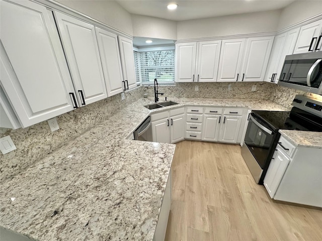 kitchen with light stone counters, light hardwood / wood-style flooring, stainless steel appliances, white cabinetry, and sink