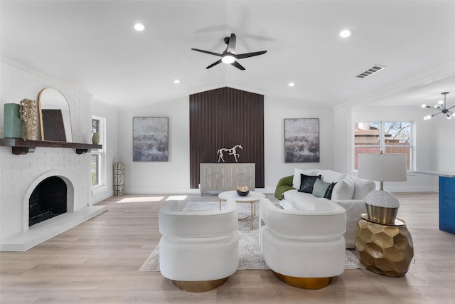 living room featuring vaulted ceiling, light hardwood / wood-style floors, ornamental molding, a fireplace, and ceiling fan with notable chandelier