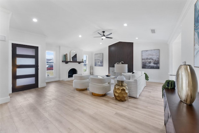 living room with a large fireplace, light wood-type flooring, ceiling fan, and crown molding