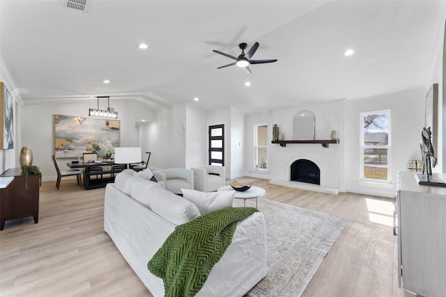 living room with ornamental molding, lofted ceiling, light wood-type flooring, a fireplace, and ceiling fan