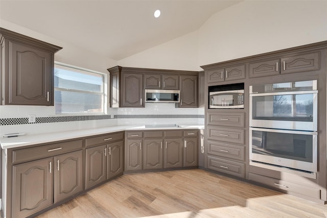 kitchen with vaulted ceiling, light hardwood / wood-style floors, decorative backsplash, appliances with stainless steel finishes, and dark brown cabinets