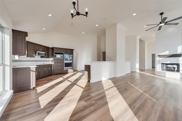 kitchen featuring light wood-type flooring, ceiling fan with notable chandelier, dark brown cabinetry, high vaulted ceiling, and appliances with stainless steel finishes