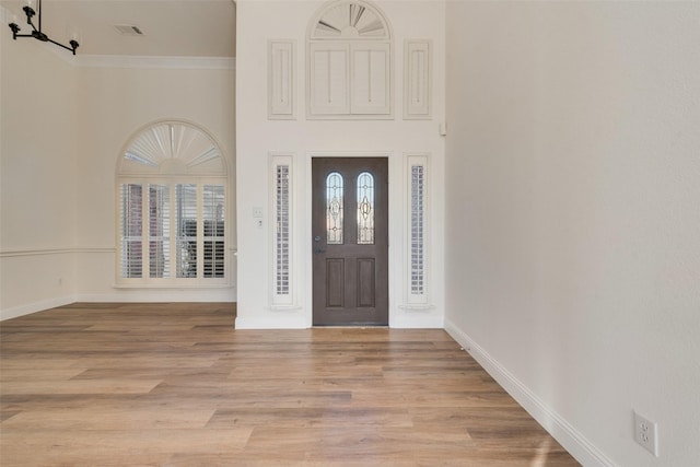 entrance foyer with a towering ceiling, crown molding, and light hardwood / wood-style flooring