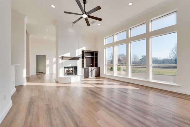 unfurnished living room featuring a large fireplace, ceiling fan, crown molding, and light hardwood / wood-style floors