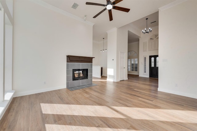 unfurnished living room with a tile fireplace, a towering ceiling, light wood-type flooring, ceiling fan with notable chandelier, and ornamental molding