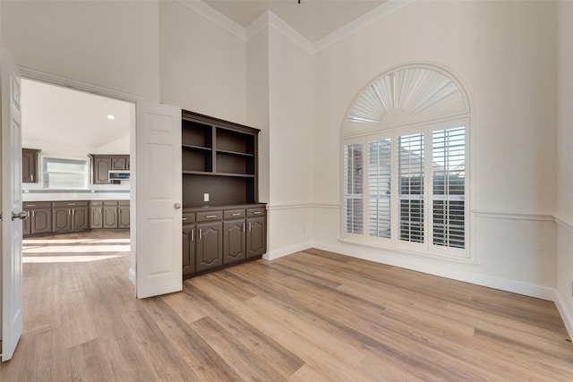 unfurnished room with a high ceiling, light wood-type flooring, and crown molding