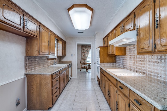 kitchen with under cabinet range hood, white appliances, a sink, light countertops, and brown cabinets