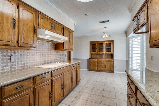 kitchen with light tile patterned flooring, under cabinet range hood, electric cooktop, brown cabinets, and pendant lighting