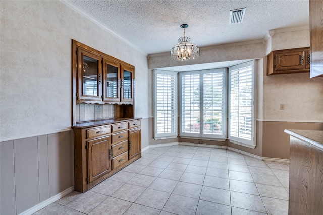 unfurnished dining area featuring a textured ceiling, light tile patterned floors, visible vents, wainscoting, and an inviting chandelier