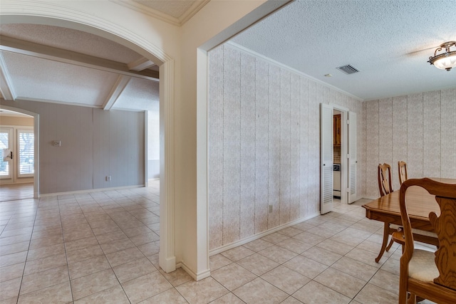 unfurnished dining area featuring arched walkways, crown molding, light tile patterned floors, a textured ceiling, and beamed ceiling