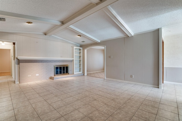 unfurnished living room with light tile patterned floors, arched walkways, a glass covered fireplace, lofted ceiling with beams, and a textured ceiling