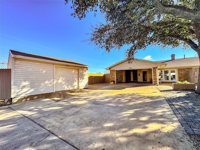 exterior space featuring driveway, a detached garage, fence, and an outbuilding