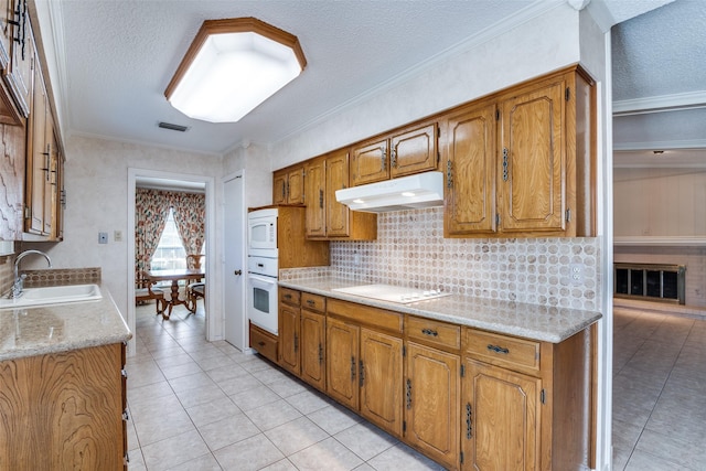 kitchen with under cabinet range hood, white appliances, a sink, visible vents, and brown cabinets