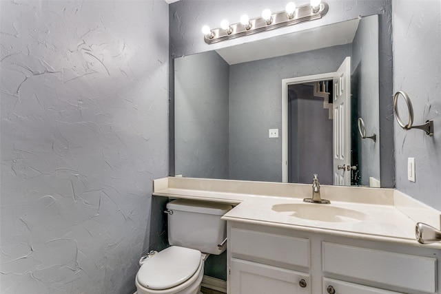 bathroom featuring toilet, a textured wall, and vanity