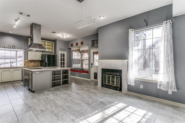 kitchen featuring visible vents, island range hood, black fridge with ice dispenser, a fireplace, and a sink