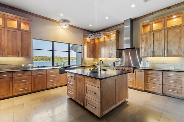 kitchen featuring a kitchen island with sink, ornamental molding, sink, wall chimney range hood, and backsplash