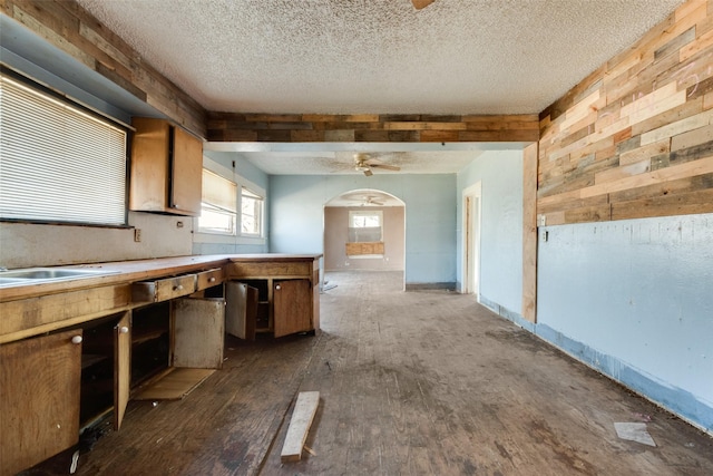 kitchen with sink, a textured ceiling, ceiling fan, wood walls, and dark wood-type flooring