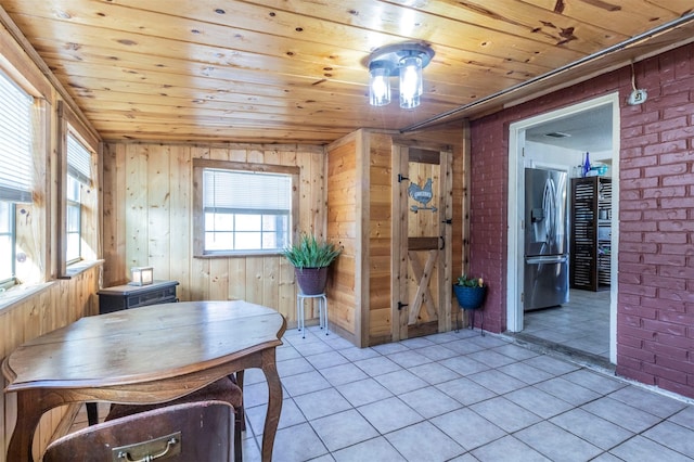 tiled dining space featuring a healthy amount of sunlight, wood ceiling, and brick wall