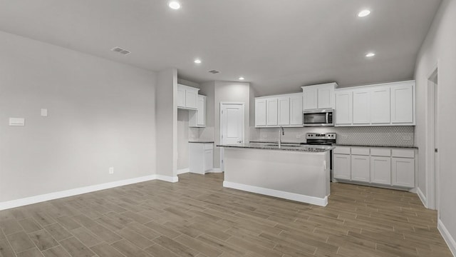 kitchen with stainless steel appliances, white cabinetry, and a center island with sink