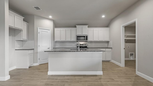 kitchen featuring a kitchen island with sink, white cabinets, dark stone counters, appliances with stainless steel finishes, and sink