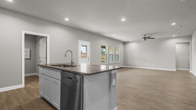 kitchen featuring dark stone countertops, a center island with sink, ceiling fan, sink, and stainless steel dishwasher