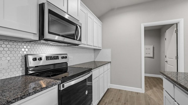 kitchen featuring appliances with stainless steel finishes, white cabinetry, dark stone countertops, and backsplash