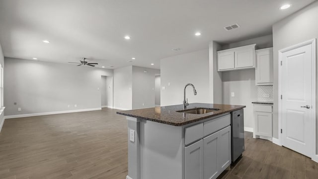 kitchen with dishwasher, dark stone countertops, a center island with sink, ceiling fan, and sink