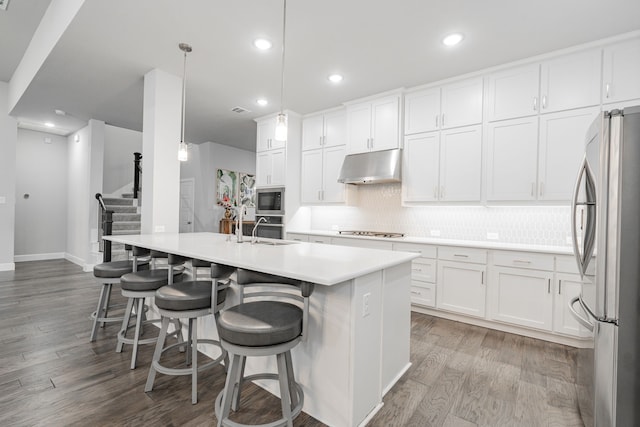 kitchen featuring decorative light fixtures, a center island with sink, a breakfast bar, white cabinets, and appliances with stainless steel finishes