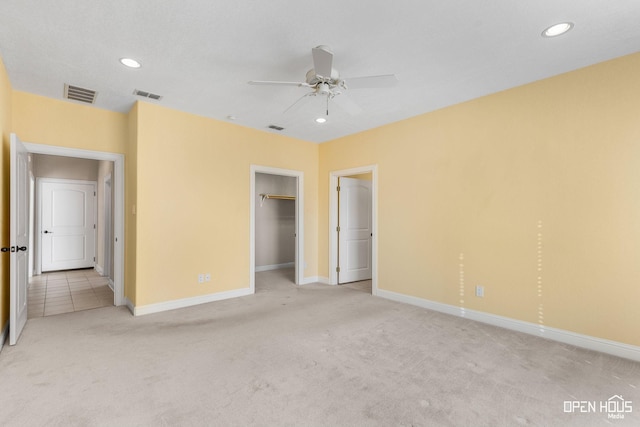 unfurnished bedroom featuring a walk in closet, light colored carpet, ceiling fan, and a closet