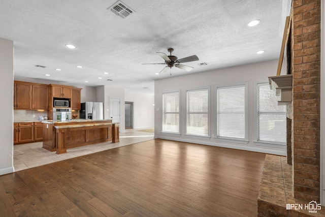 kitchen with a textured ceiling, light hardwood / wood-style flooring, stainless steel appliances, a kitchen island, and ceiling fan