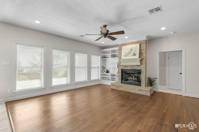 unfurnished living room with hardwood / wood-style flooring, a textured ceiling, built in shelves, a fireplace, and ceiling fan