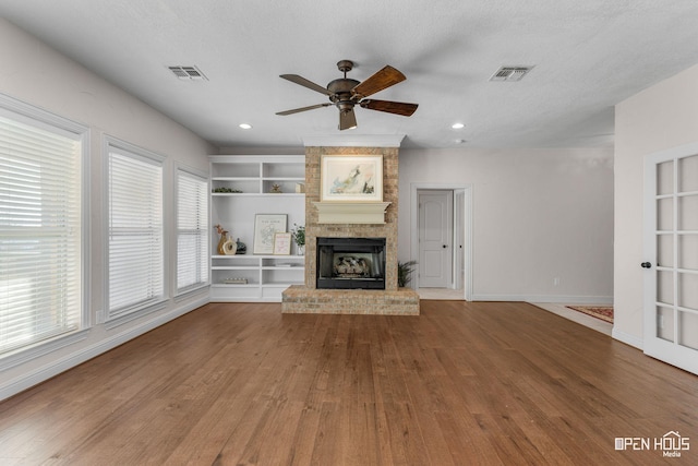 unfurnished living room featuring a textured ceiling, ceiling fan, built in shelves, and wood-type flooring