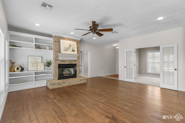 unfurnished living room with a textured ceiling, french doors, ceiling fan, a brick fireplace, and built in shelves