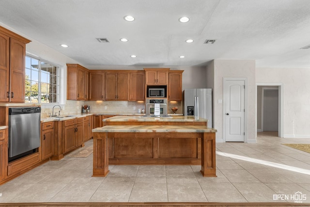 kitchen with appliances with stainless steel finishes, a center island, sink, light tile patterned flooring, and tasteful backsplash