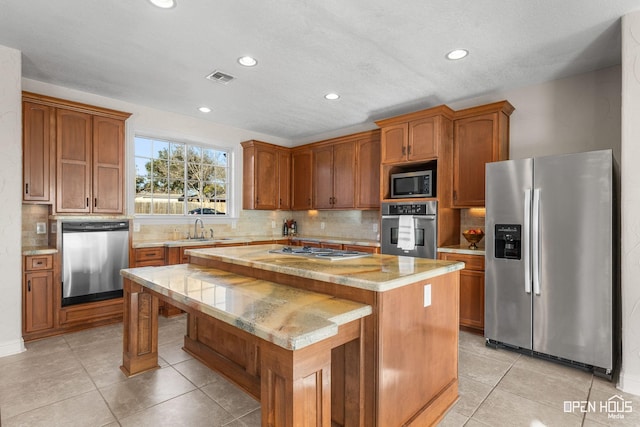 kitchen featuring stainless steel appliances, sink, tasteful backsplash, light tile patterned floors, and a kitchen island