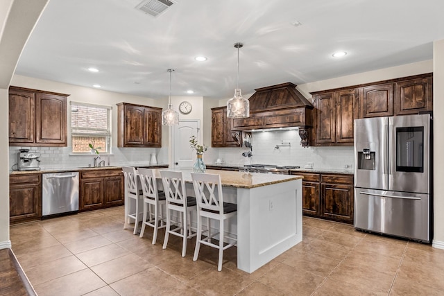 kitchen featuring custom exhaust hood, pendant lighting, a center island, appliances with stainless steel finishes, and sink