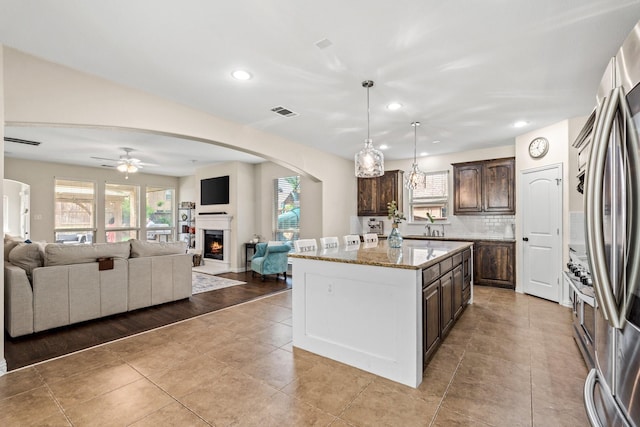 kitchen with ceiling fan, decorative backsplash, dark brown cabinetry, a kitchen island, and pendant lighting