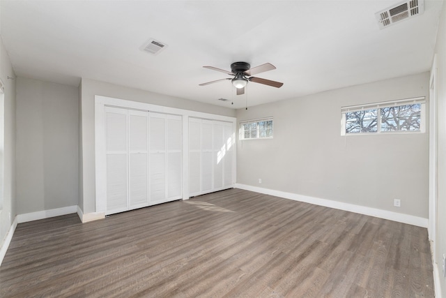 unfurnished bedroom featuring ceiling fan, two closets, and dark hardwood / wood-style floors