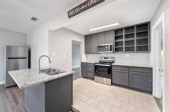 kitchen featuring light stone countertops, decorative backsplash, gray cabinets, appliances with stainless steel finishes, and sink