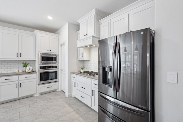 kitchen featuring stainless steel appliances, light tile patterned floors, white cabinets, and backsplash